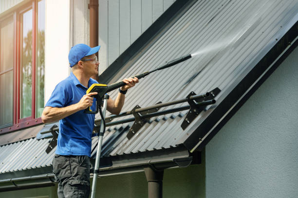 Man standing on ladder and cleaning house metal roof with high pressure washer